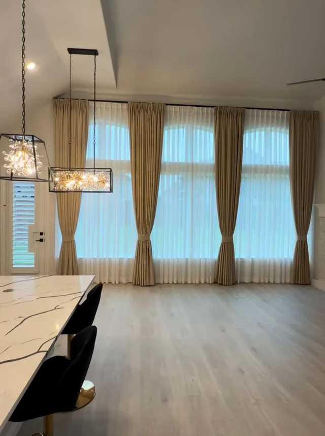 Beige tieback drapes and white sheers along tall windows beside a kitchen island.